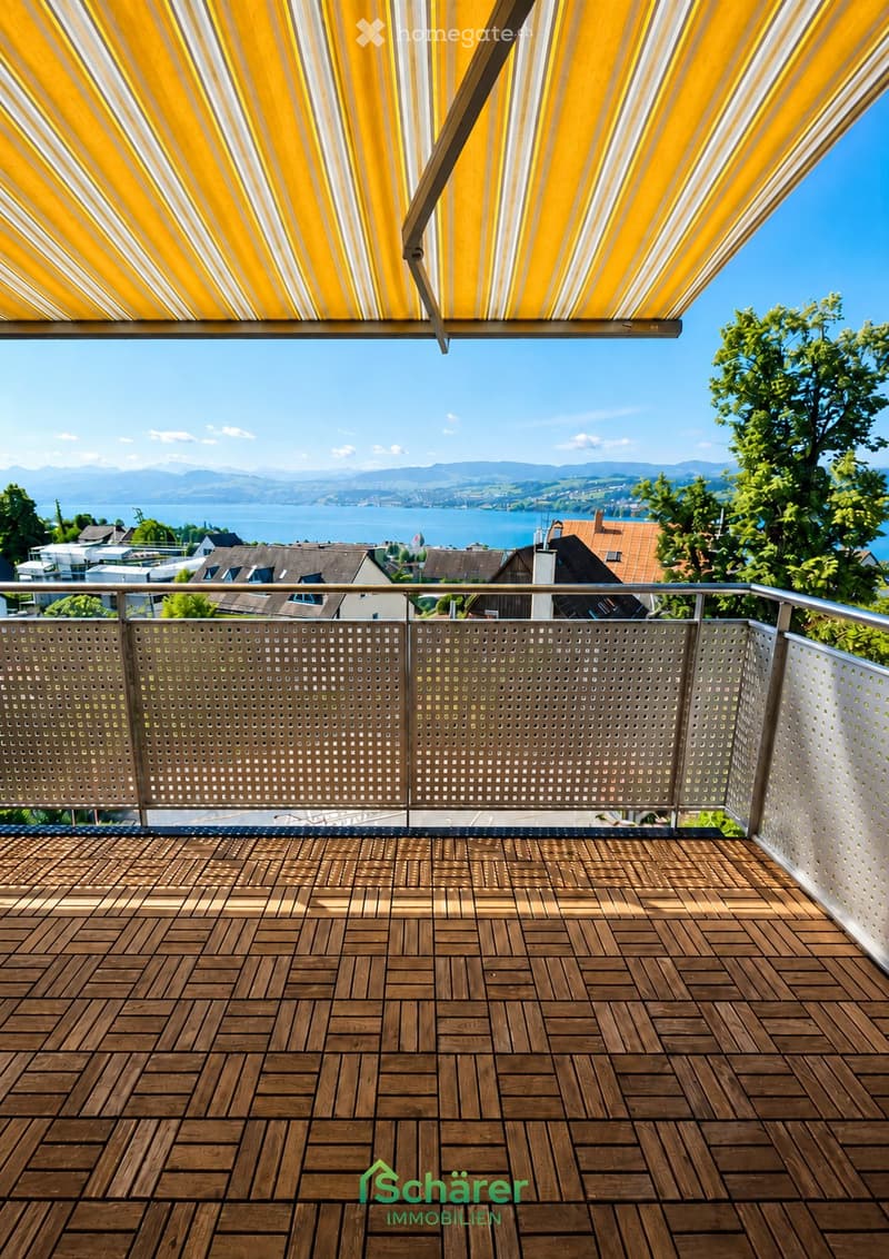 Wooden deck with a modern railing and a retractable awning, overlooking a scenic lake and distant mountains.