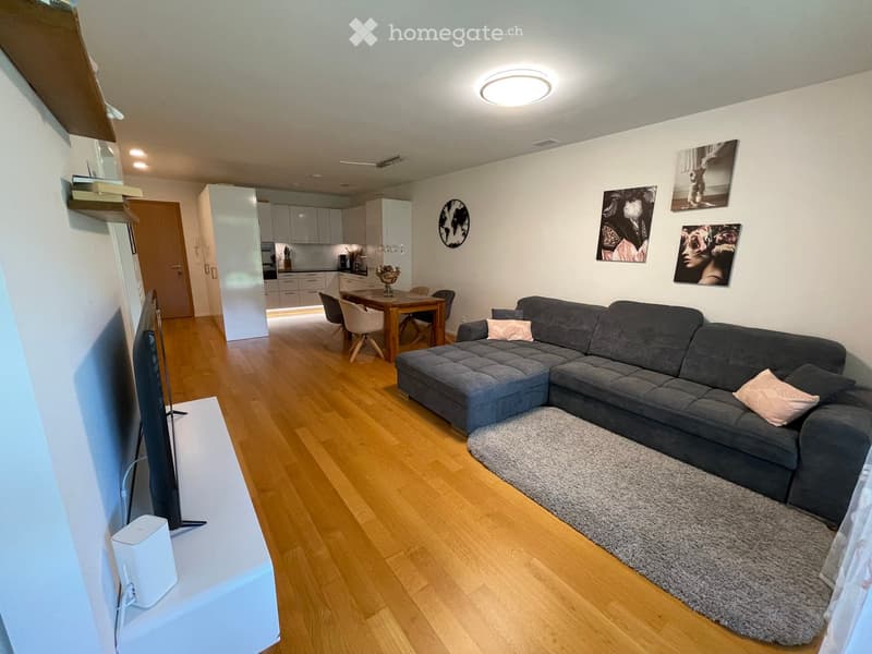 Modern living room with a grey sectional sofa, coffee table, dining area with chairs and table, and a flat-screen TV on a stand.