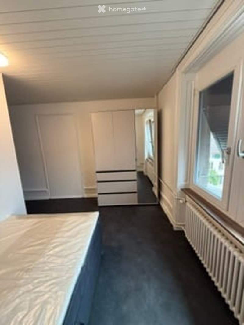 Empty room with white walls, wooden floor, large window, and built-in closet with drawers.