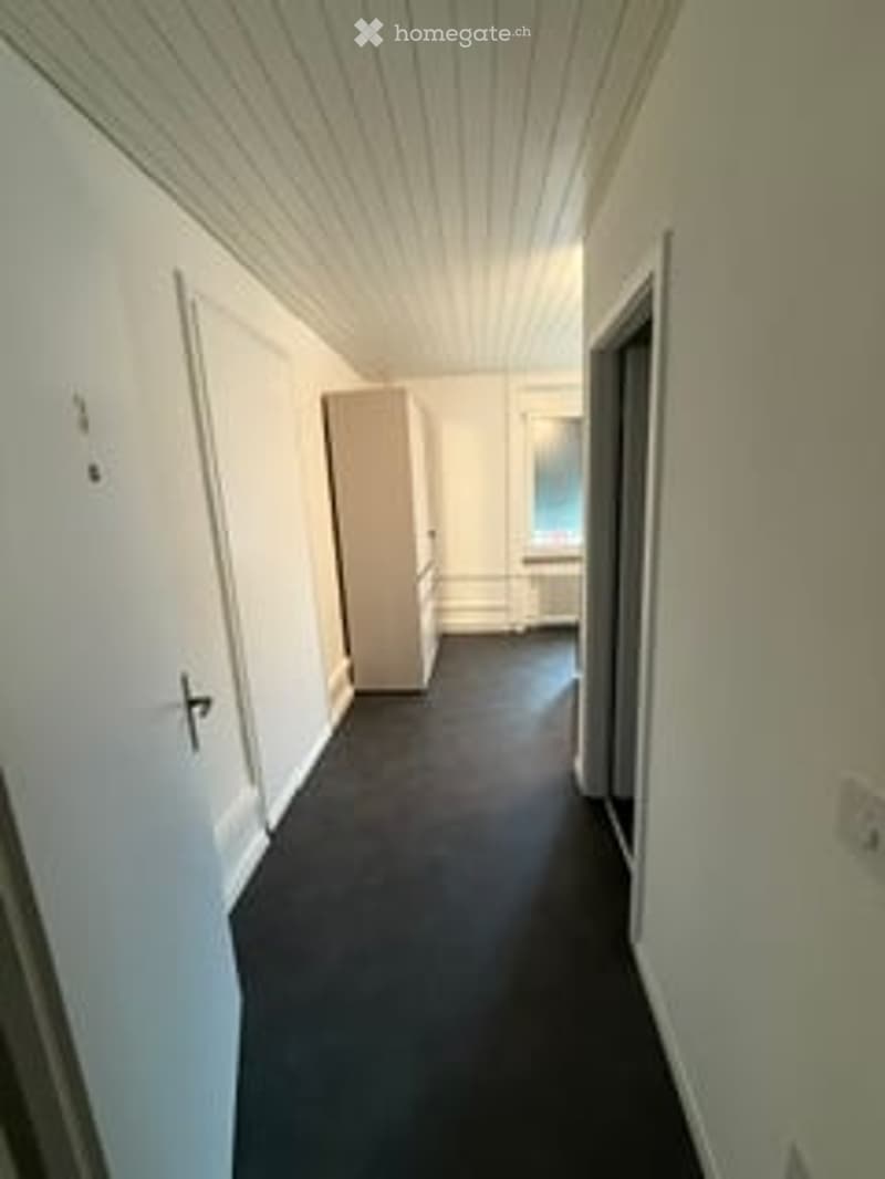 Empty hallway with white walls, dark carpeted floor, and a single closed door on the left side.