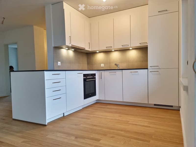 Modern kitchen with white cabinets, stainless steel appliances, and wooden flooring.