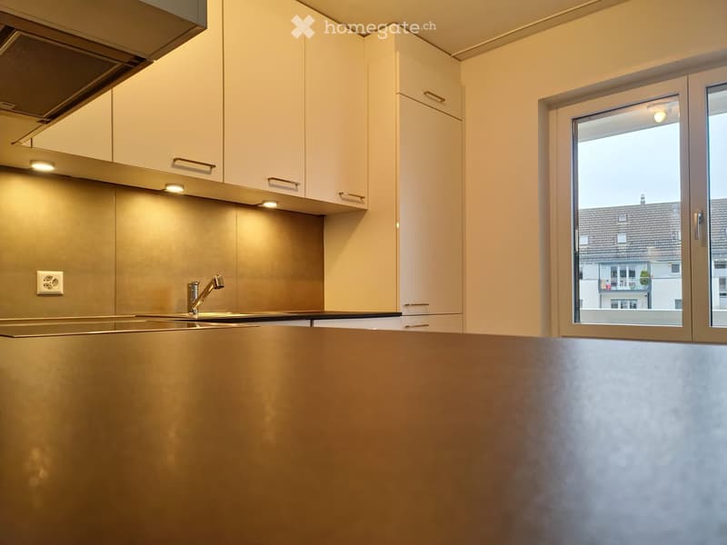 Modern kitchen with light-colored cabinets, a stainless steel sink, and a sleek faucet. The space features built-in lighting and a large window offering a view of the exterior.