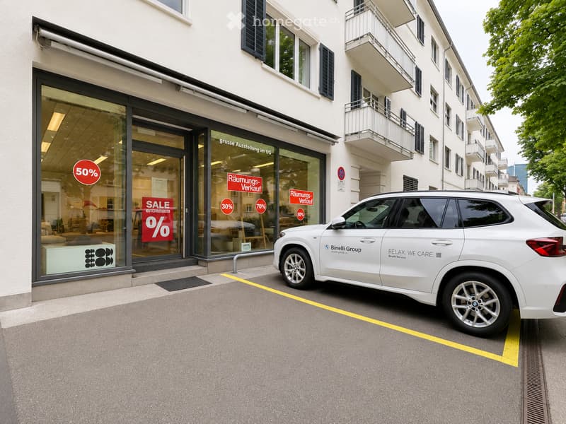 A multi-story building with a storefront displaying large sale signs, including a 50% discount. A white SUV is parked in front of the building.