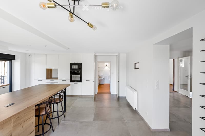 Modern kitchen with white cabinets, wooden table, stools, microwave, oven, and radiator.