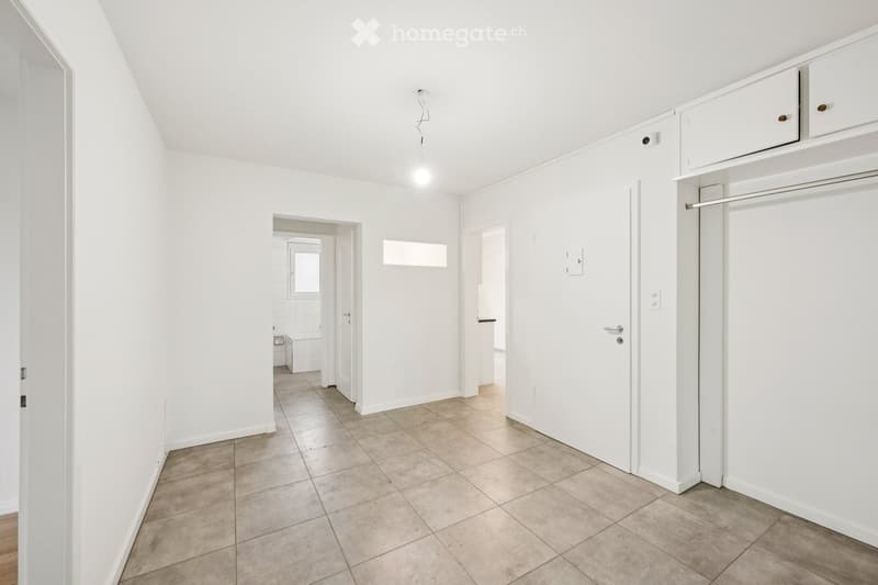 Empty hallway with white walls, tiled floor, and several doors leading to other rooms.