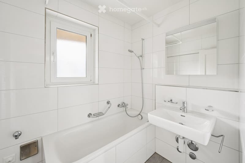 Modern bathroom with white tiles, a bathtub, a sink, a large mirror, and a showerhead.