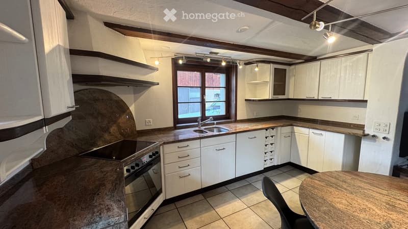 Modern kitchen with white cabinets, granite countertops, stainless steel sink, and built-in oven. Features a large window with wooden frame and wooden ceiling beams.