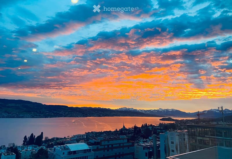 Balcony / Terrace. Panoramic view from a balcony or terrace overlooking a lake and cityscape at sunset, with mountains in the background.