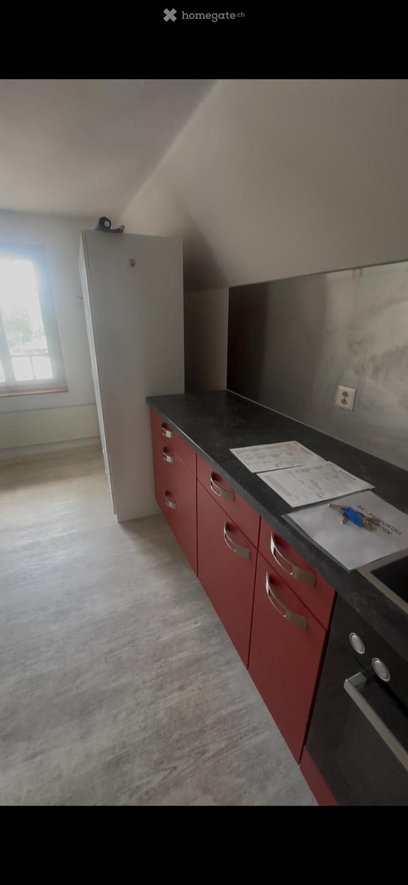 Modern kitchen with red cabinets, black countertop, and built-in oven. Papers and keys are placed on the counter.