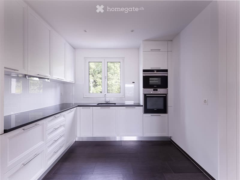 Modern kitchen with white cabinets, black countertops, and stainless steel appliances including an oven and sink.