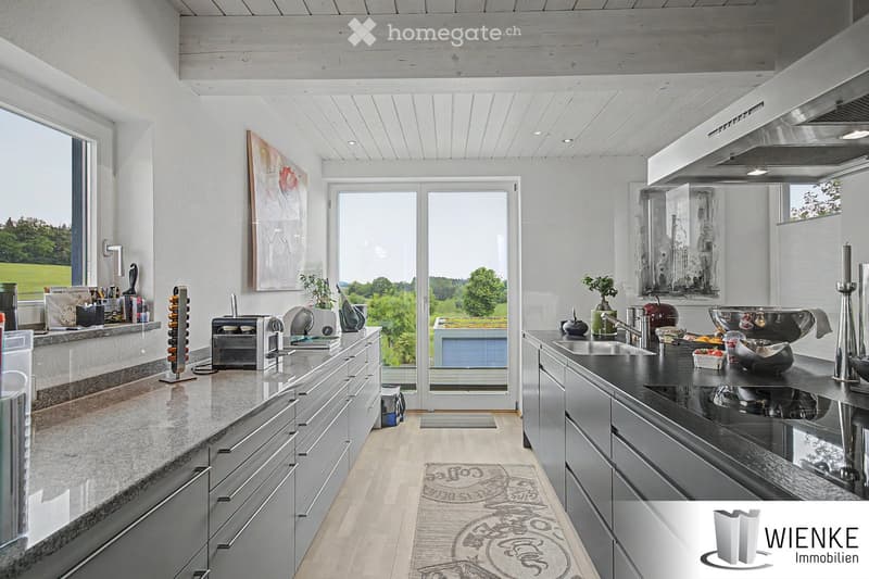Modern kitchen with white cabinets, granite countertops, stainless steel appliances, and large windows overlooking a green landscape.