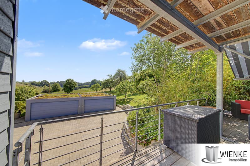 Balcony with metal railing, tiled floor, wicker storage box, red bench, and a view of a green landscape with trees and hills.