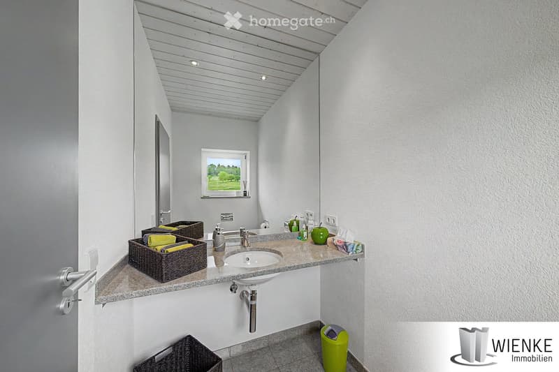 Modern bathroom with a double sink, wicker baskets holding towels, a mirror, and a window offering a view of greenery.