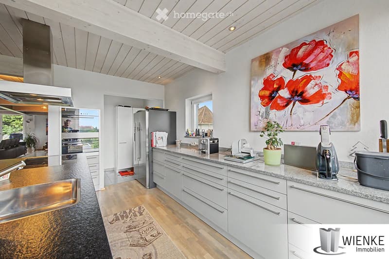Modern kitchen with white cabinets, granite countertops, stainless steel appliances, and a large window offering a view of the outdoors.