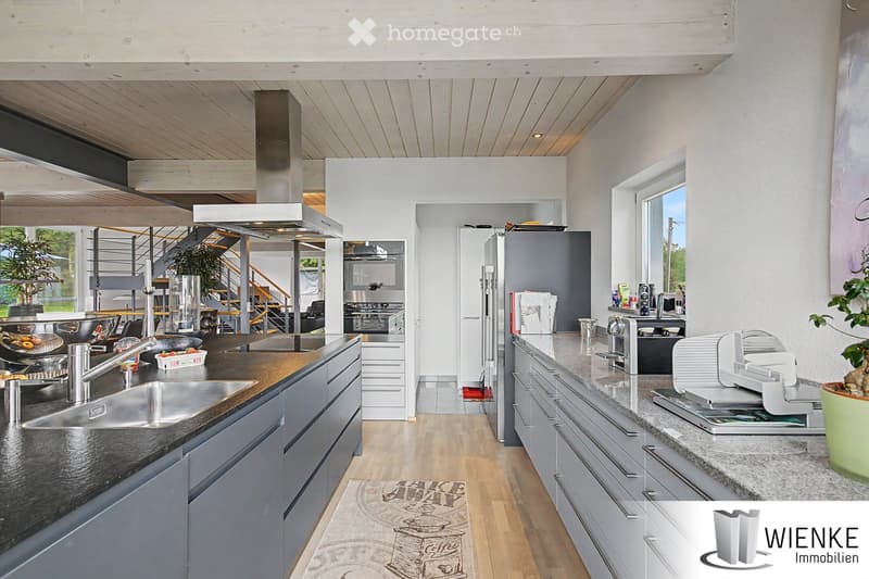 Modern kitchen with stainless steel appliances, granite countertops, and wooden flooring. Features include a large island, built-in cabinets, and a range hood.