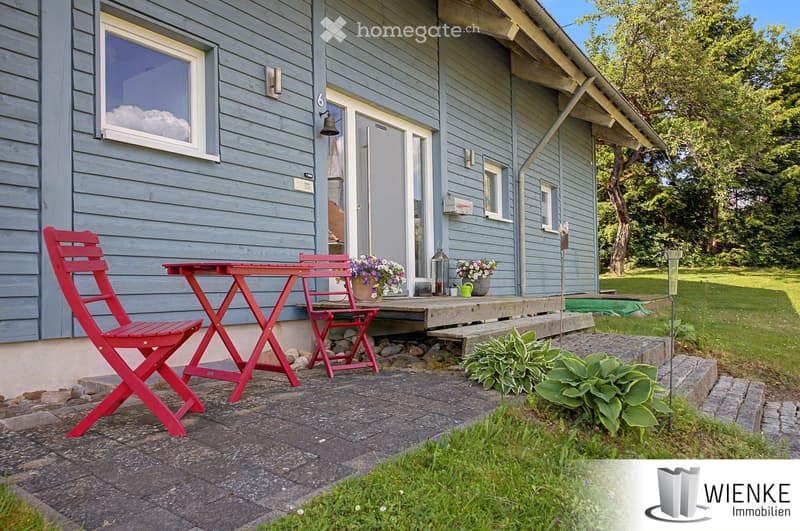 Outdoor patio area with a red table and chairs, potted plants, and a small garden near a house entrance.