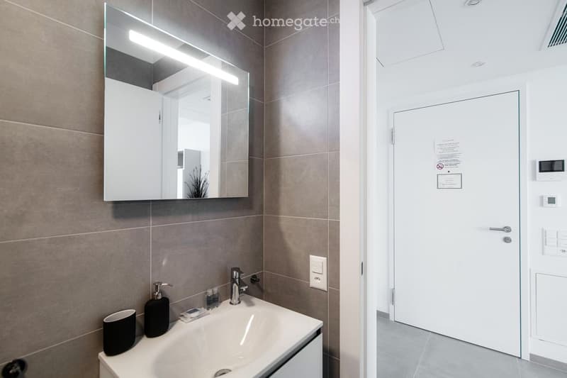 Modern bathroom with a white sink, chrome faucet, mirror with built-in lighting, and a black cup on the counter.