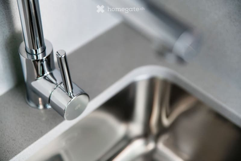 Close-up of a modern chrome faucet with dual handles and a sleek design, mounted on a grey countertop.