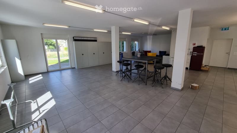 Bright, open room with tiled floor, large sliding glass door leading to outdoor area, table with stools, cabinets, and refrigerator.