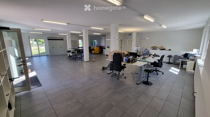 Office space with tiled floor, large windows, several chairs, tables, and a screen.