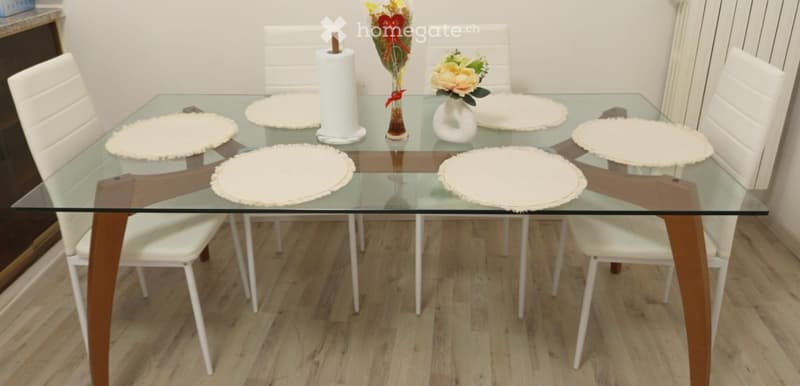 Glass dining table with six white chairs, placemats, and a vase with flowers.