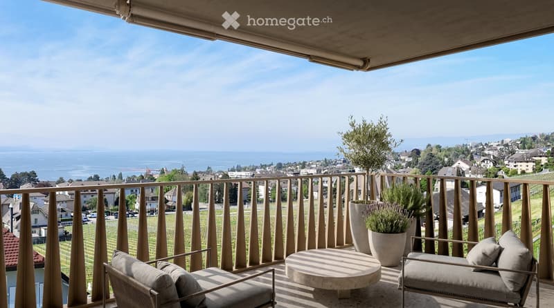 Balcony with a scenic view of a lake and town, featuring a round table, two chairs, and potted plants.