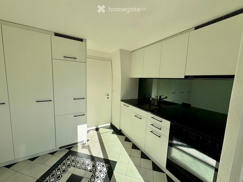 Modern kitchen with white cabinets, black countertops, and a tiled floor. Features a sink, faucet, and oven.