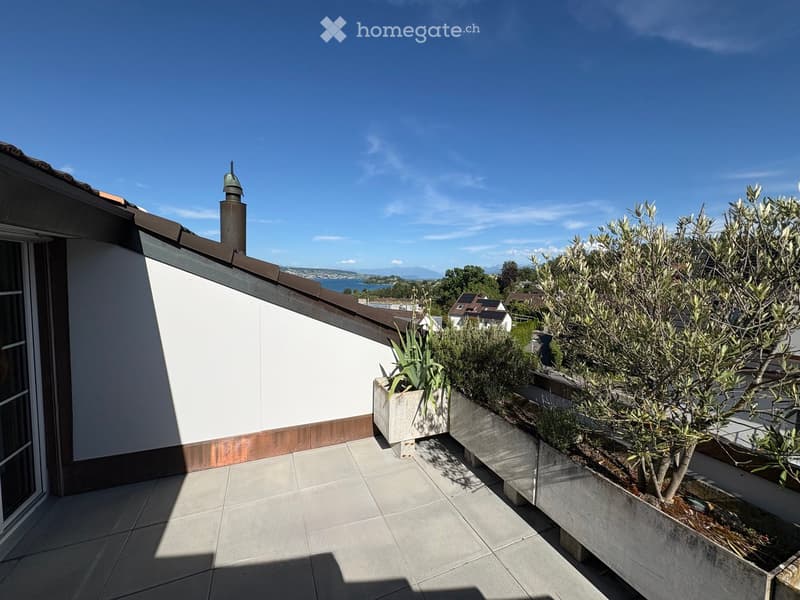 Roof terrace with tiled flooring, white wall, and potted plants, overlooking a scenic lake and distant mountains.