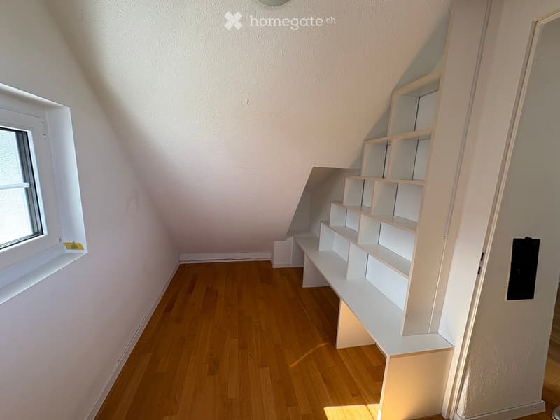 Empty room with wooden flooring, white walls, and built-in white shelving unit. A window on the left side allows natural light to enter.