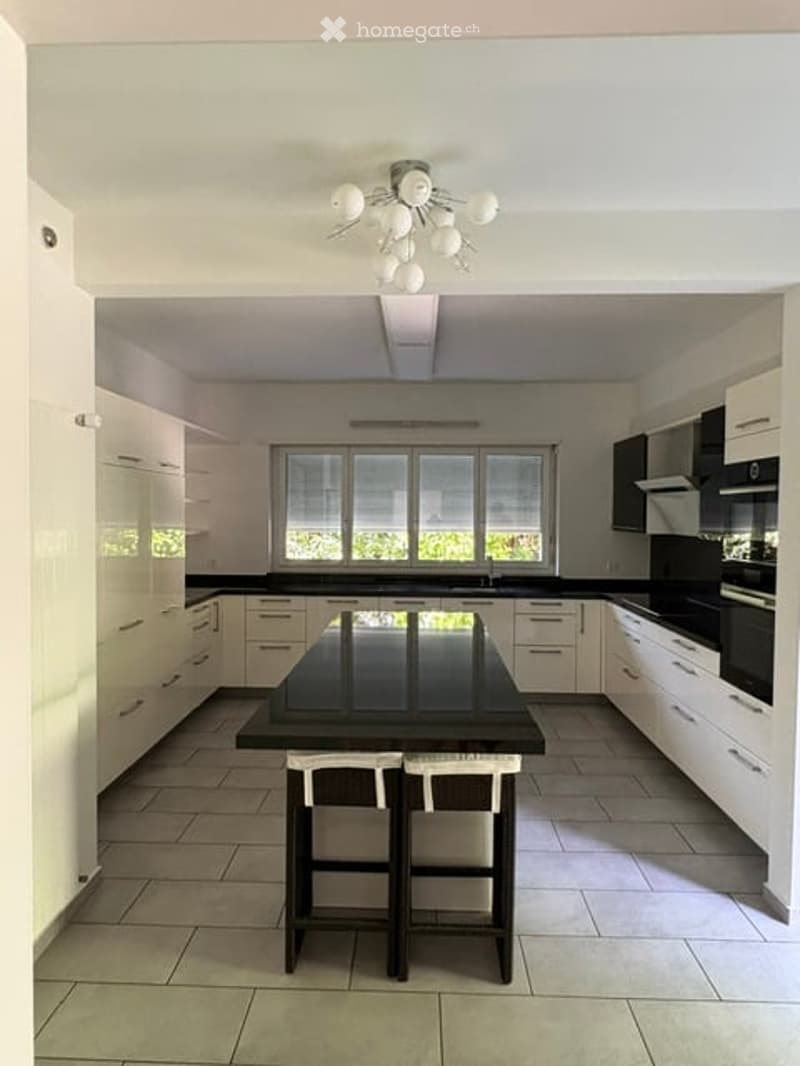 Modern kitchen with white cabinets, black island, and built-in appliances. Two stools are placed at the island.
