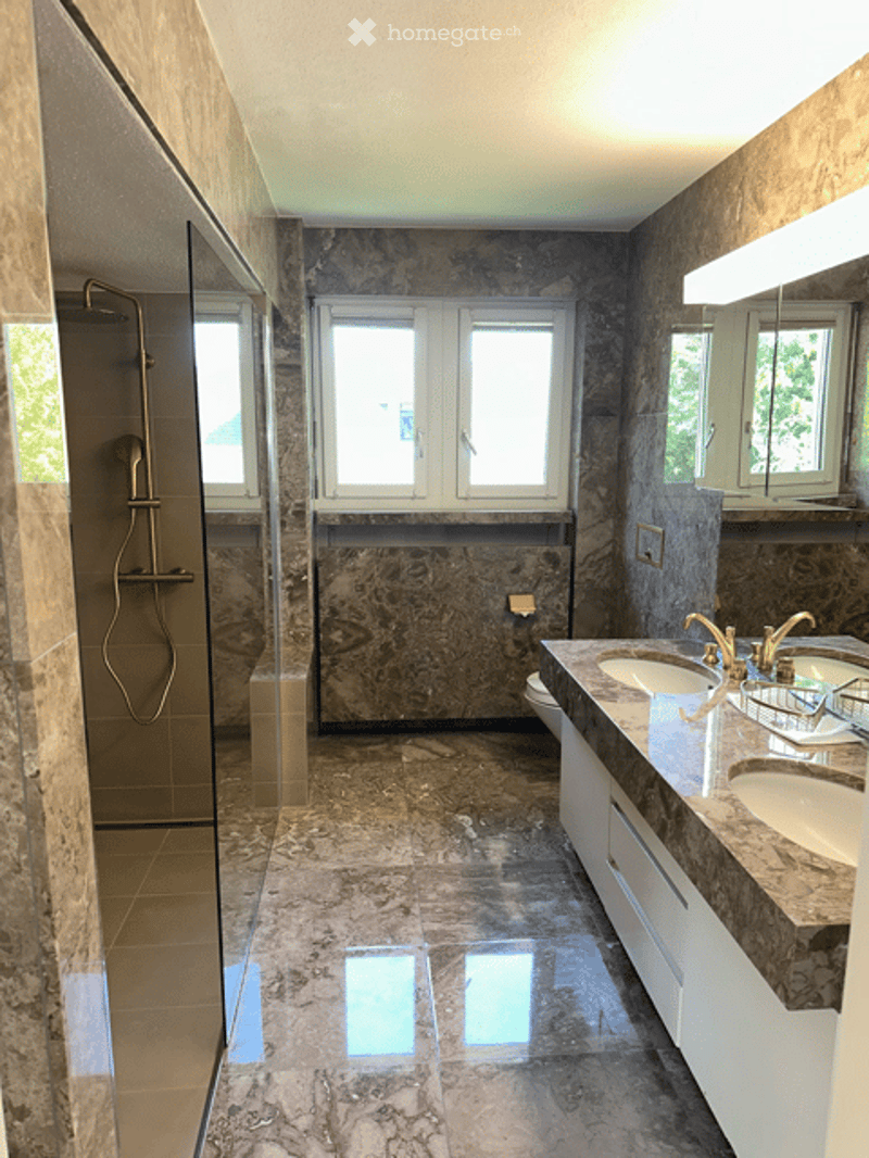 Modern bathroom with marble tiles, double sink vanity, large mirror, and separate shower area with glass enclosure.
