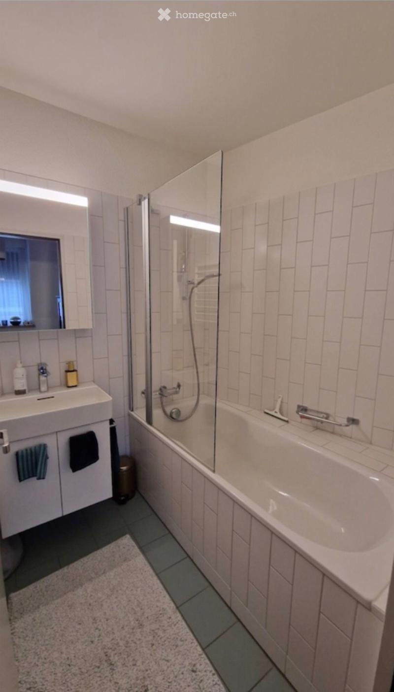 Modern bathroom with white tiles, a bathtub, a sink with a mirror, and a glass-enclosed shower area.