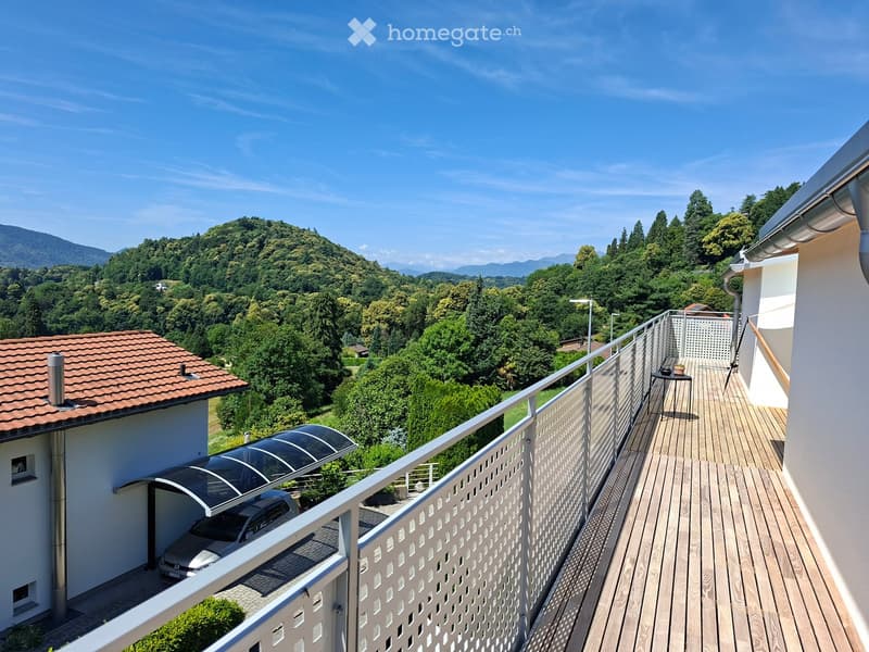 Balcony with wooden decking, metal railing, and a view of a lush green landscape and mountains.