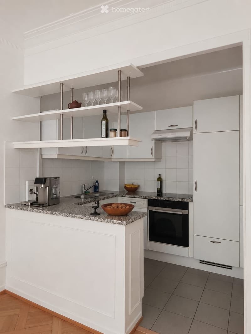 Modern kitchen with white cabinets, granite countertop, coffee maker, oven, sink, and decorative items on shelves.