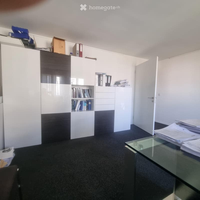 Office space with a black and white cabinet, bookshelf, glass table, and scattered papers and folders.