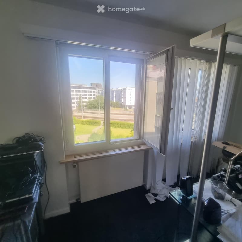 Office space with large windows, a radiator, a chair, a table, and a screen.