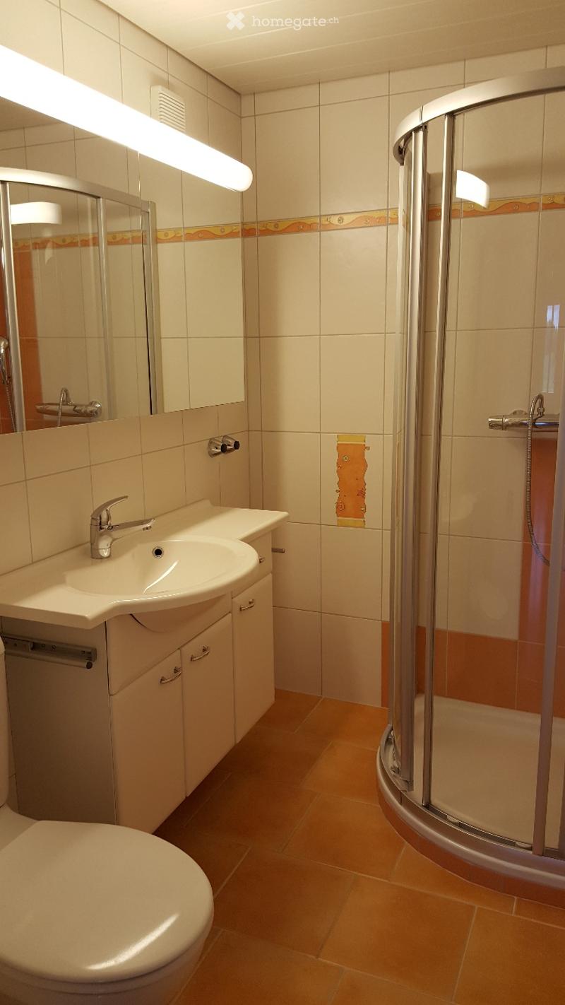 Modern bathroom with beige tiles, a white sink with a chrome faucet, a mirrored cabinet, a toilet, and a glass-enclosed shower stall.