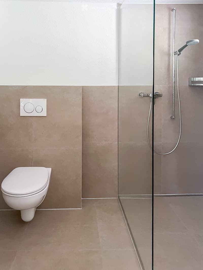 Modern bathroom with a toilet, glass-enclosed shower, and beige tiles.