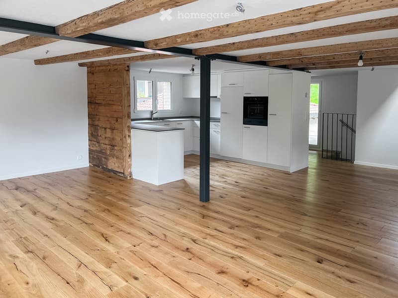 Open-plan kitchen and living area with white cabinets, a central island, wooden flooring, and exposed wooden beams on the ceiling.
