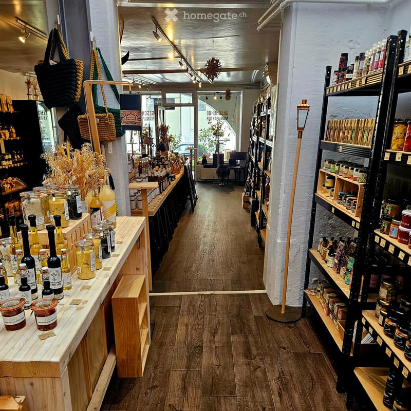A well-lit store with wooden shelves displaying various bottles and jars of food products, wooden tables, and hanging handbags.