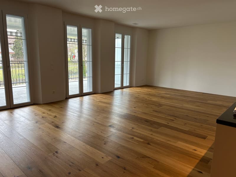Empty room with wooden flooring, large glass doors leading to a balcony, and white walls.