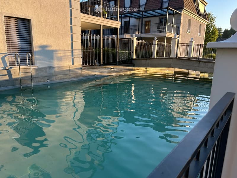 A swimming pool with clear water is situated in front of a modern building with balconies and railings.