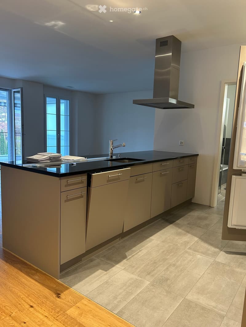Modern kitchen with a central island, stainless steel range hood, and sleek cabinetry. Features a black countertop, a sink with a modern faucet, and a tiled floor.
