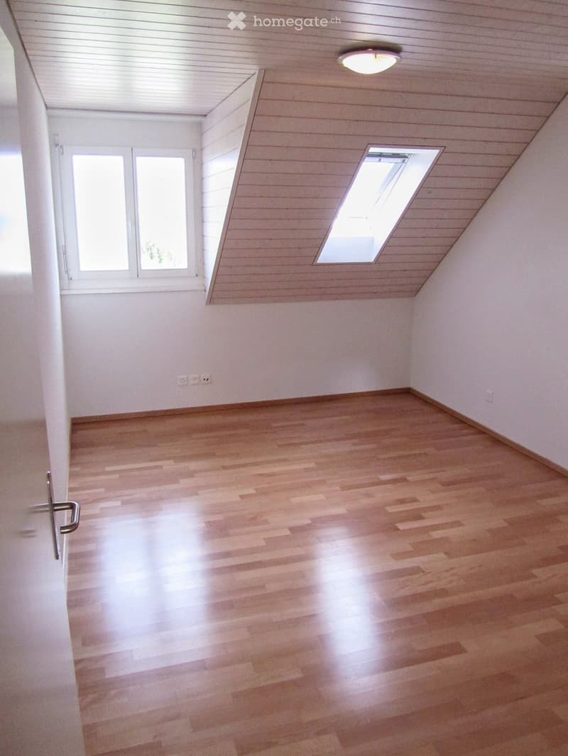 Empty room with wooden flooring, white walls, and large windows, including a skylight.