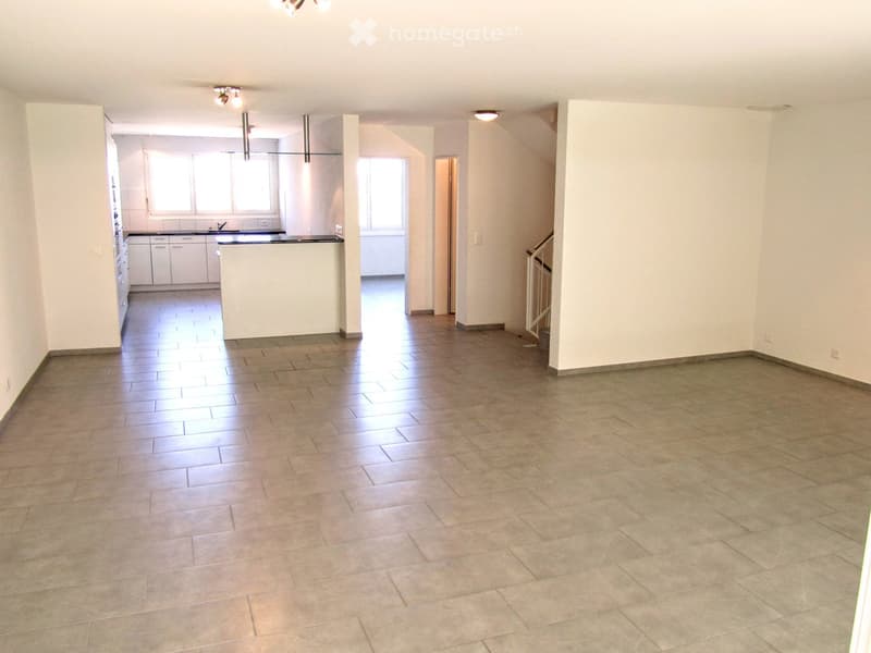 Empty room with tiled floor, white walls, and a kitchen area visible in the background. No furniture or equipment present.
