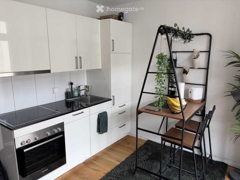 Modern kitchen with white cabinets, black countertop, sink, oven, and a small dining area with a table and chairs.