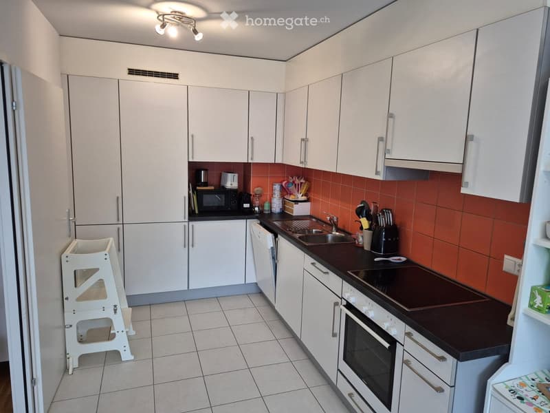 Modern kitchen with white cabinets, dark countertops, stainless steel appliances, and a small white stool near the refrigerator.