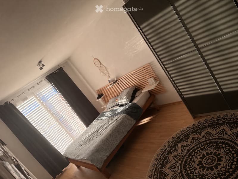 Cozy bedroom with a wooden bed, patterned bedding, nightstand, large mirror, and a round patterned rug on the floor.