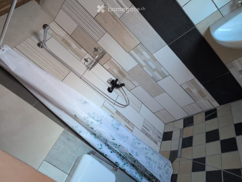 Modern bathroom with a bathtub, shower curtain, and a toilet. The floor features a mix of light and dark tiles, and the bathtub has a sleek chrome faucet.