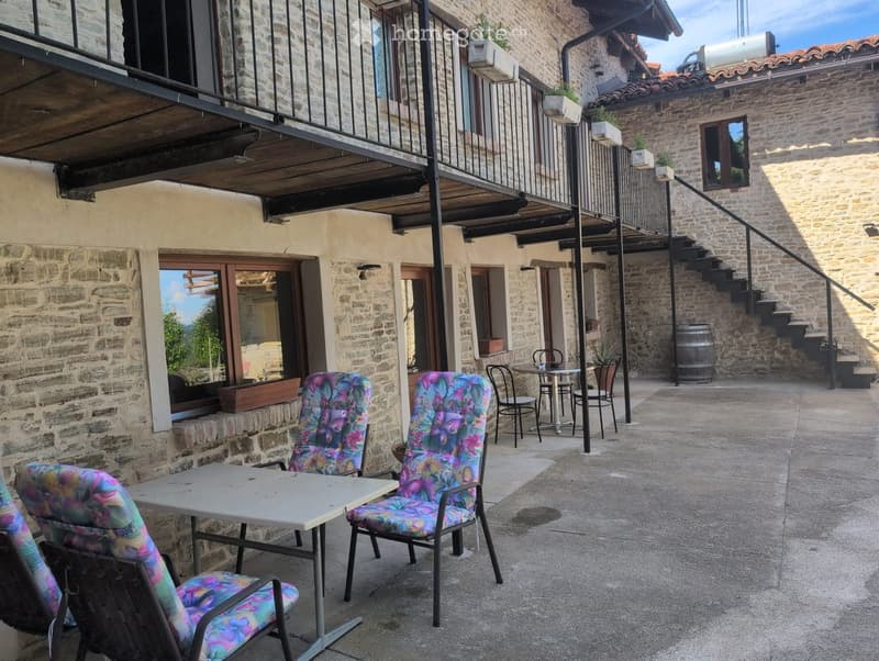 Courtyard with stone walls, outdoor seating area including a table and colorful chairs, small staircase leading to an upper level, and a barrel near the steps.